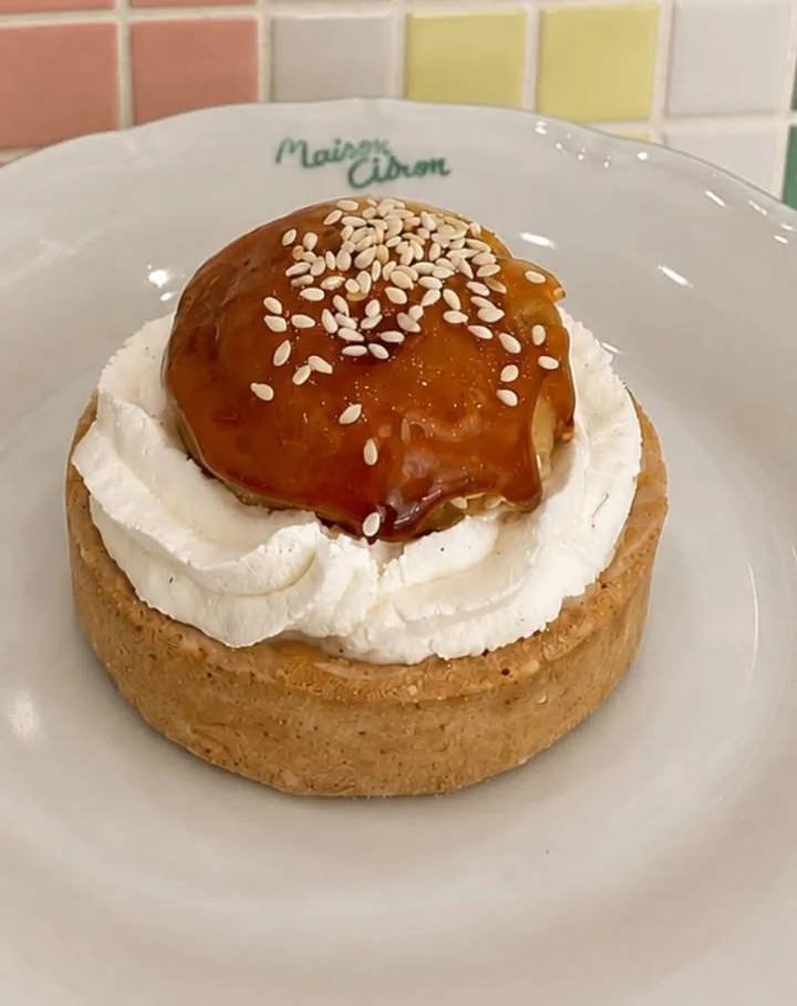 Tartelette au chou caramélisé et sésame, crème fouettée, sur assiette signée Maison Citron devant un mur de carreaux pastel.