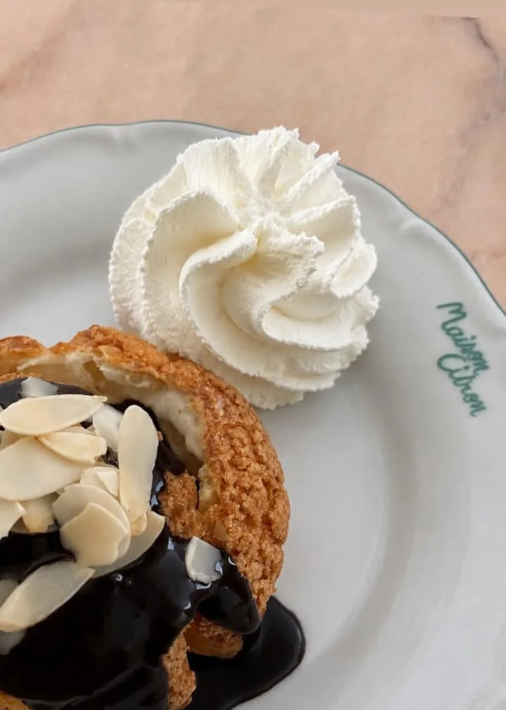 Profiterole, sauce chocolat et amandes effilées, crème à côté, sur marbre rose.